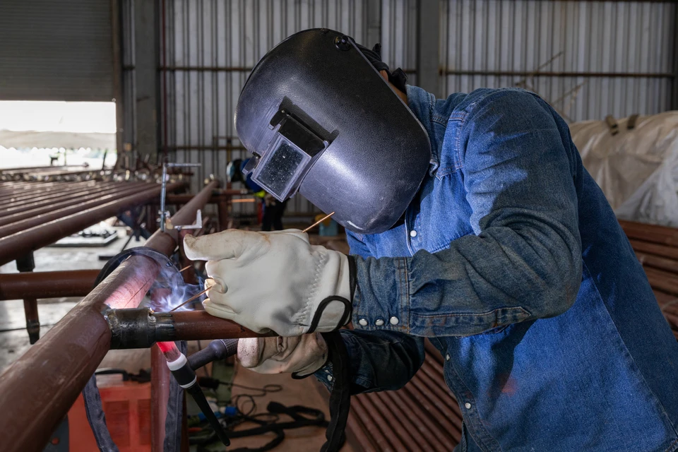 Atelier intérieur avec artisan soudeur portant masque de protection et gants de sécurité, travaillant sur pièces métalliques